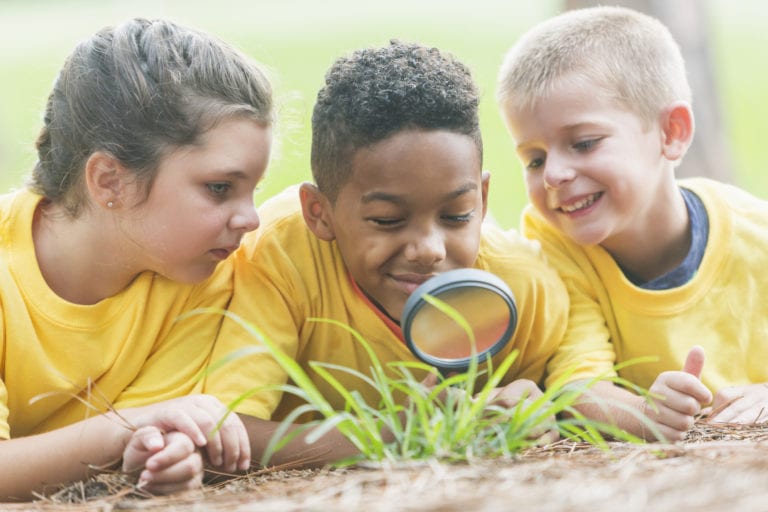 Three children exploring nature with a magnifying glass