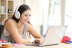 Student with headphones watches video on laptop at home