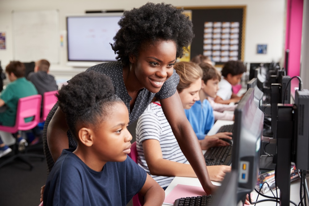 teacher helping female student working on computer in computer science class